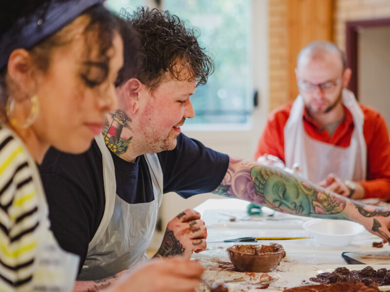 A group of friends seated at a table together try some chocolate making using piping bags 